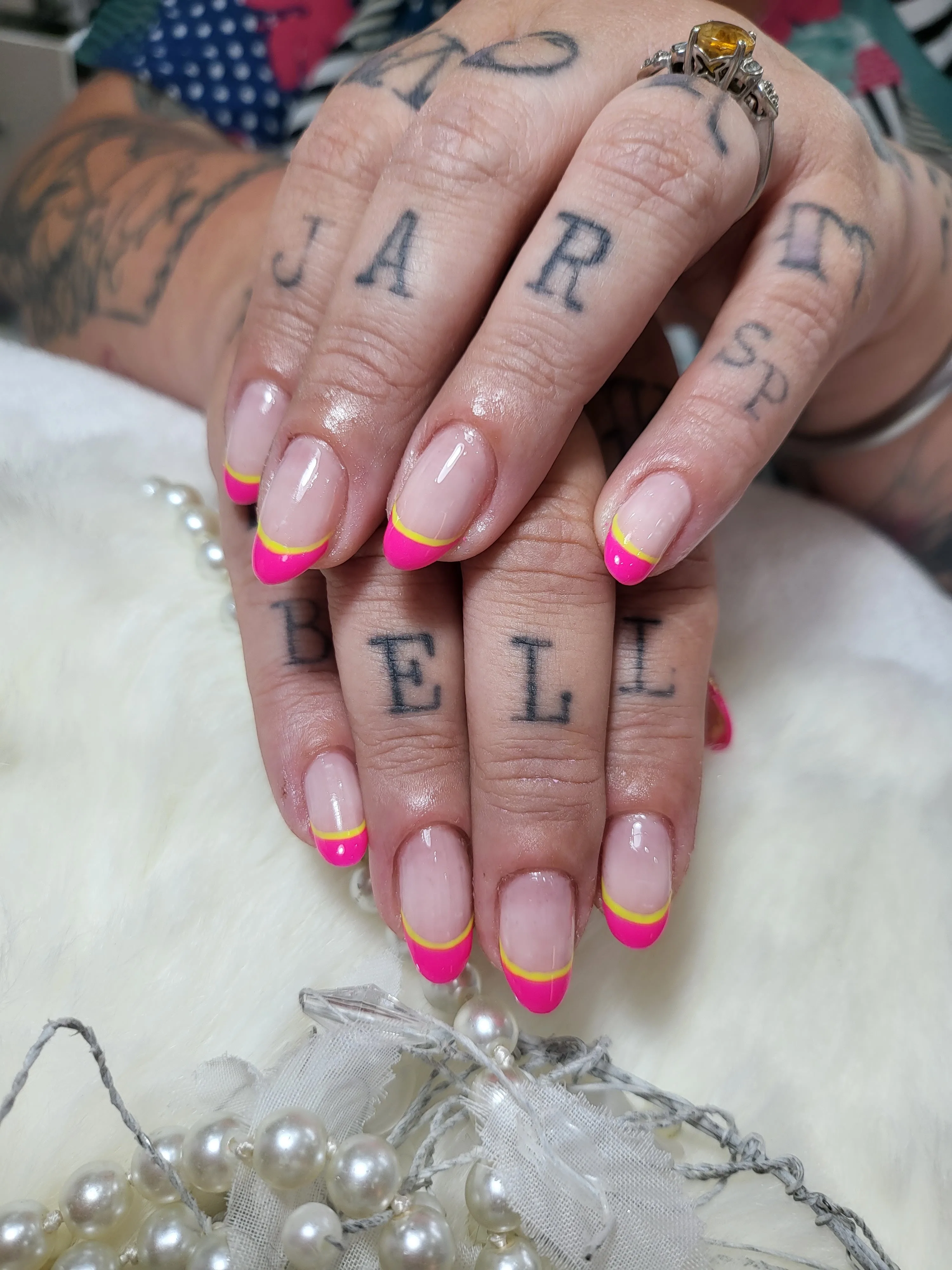 Neon-pink and yellow french tips on tattooed hands