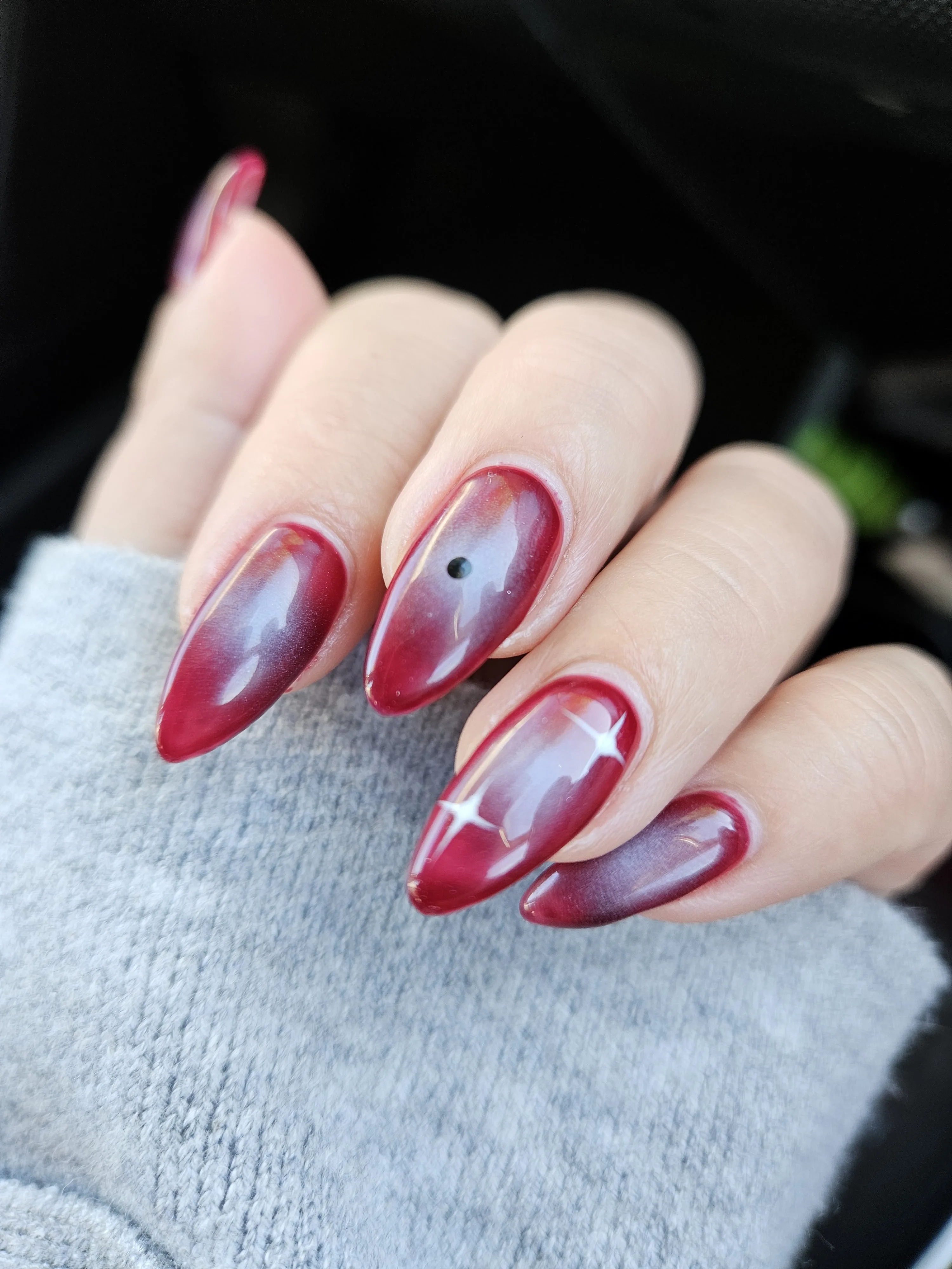 Burgundy cat-eye almond nails on a grey knit sleeve