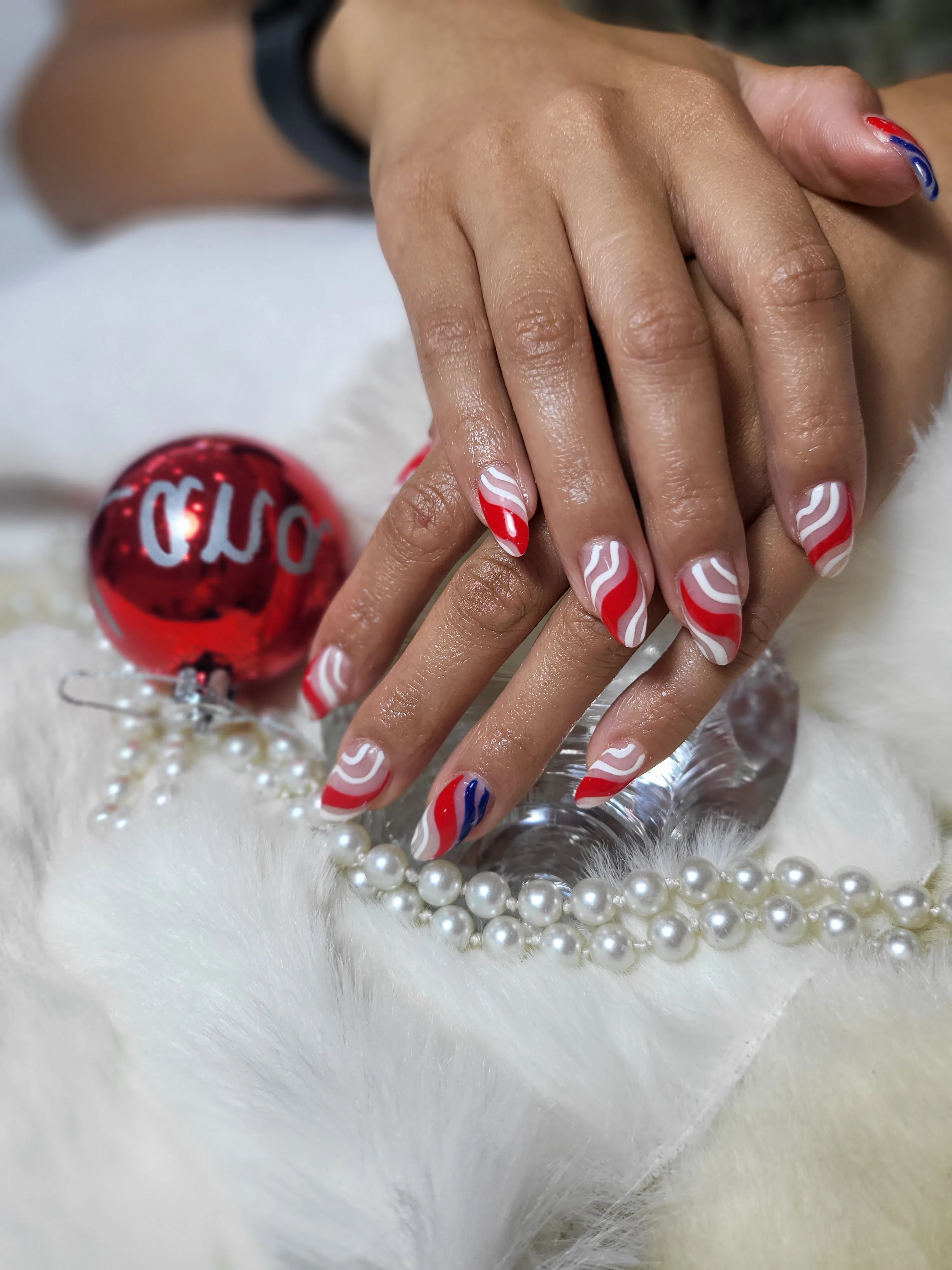 Red and white candy-swirl nails beside a red Christmas bauble