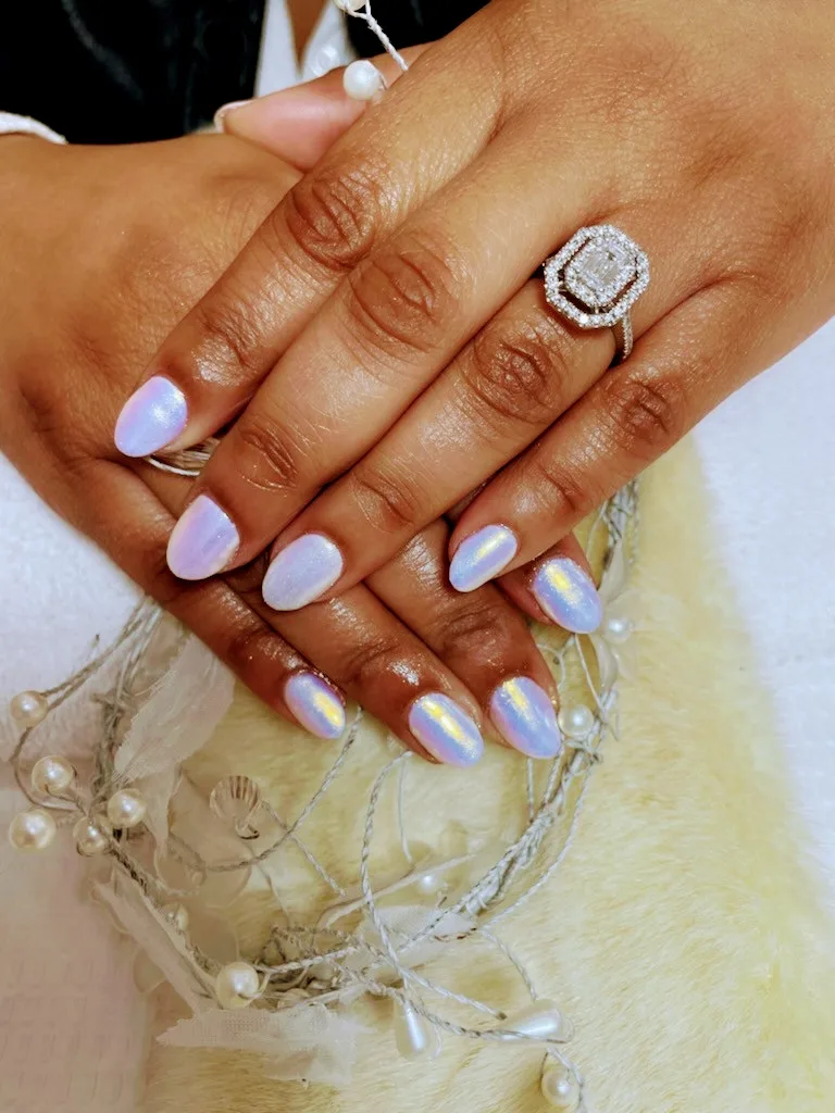 Iridescent pearl-lilac nails over white fur with diamond ring
