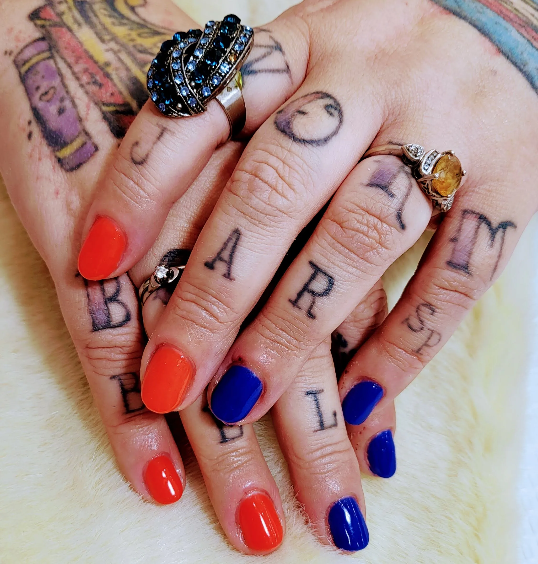 Solid orange and blue nails on tattooed hands with rings